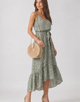 Woman wearing a green floral dress holding a round beige bag on a white background