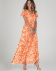 Woman wearing an orange floral dress on a gray background