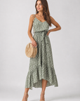 Woman wearing a green floral dress holding a woven bag on a white background
