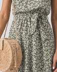 Person wearing a green floral dress holding a woven bag against a neutral background